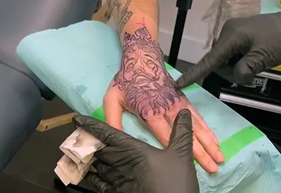 Artiste tatoueur travaillant sur un tatouage détaillé sur la main d'un client